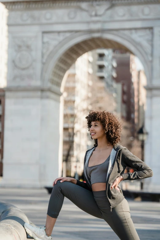 a woman standing on top of a skateboard in front of a building, a statue, trending on unsplash, arabesque, wearing a track suit, archway, nyc, black curly hair