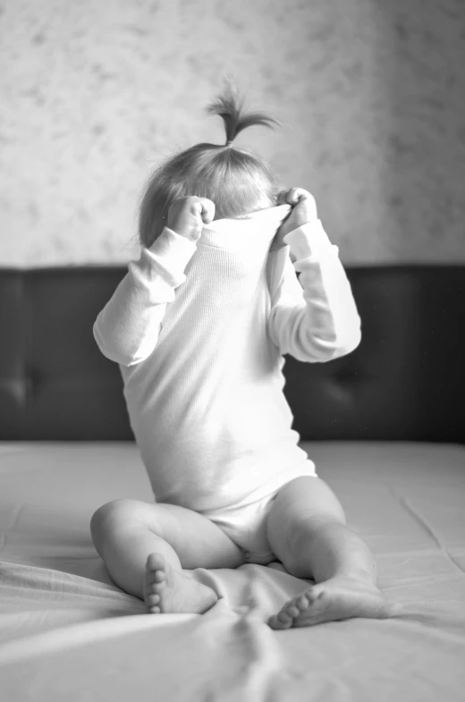 a black and white photo of a baby sitting on a bed, pixabay contest winner, happening, face covered, hair over face, white clothes, playing