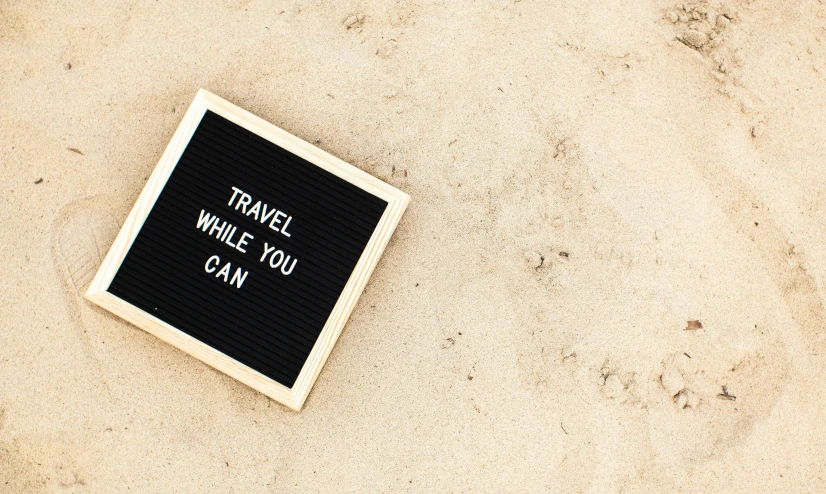 a black board with the words travel while you can written on it, pexels contest winner, sand, minimalistic aesthetics, instagram post, white