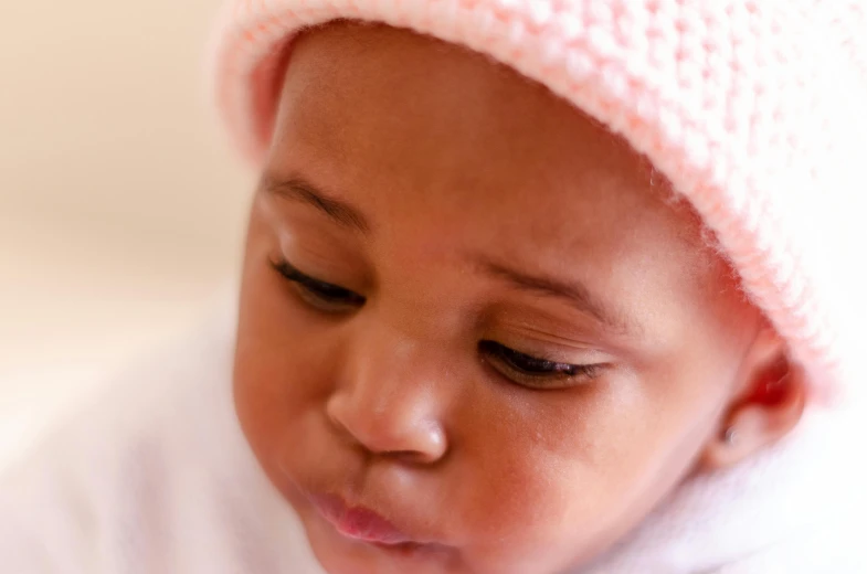 a close up of a baby wearing a pink hat, unsplash, african sybil, thoughtful, ilustration, knitted hat