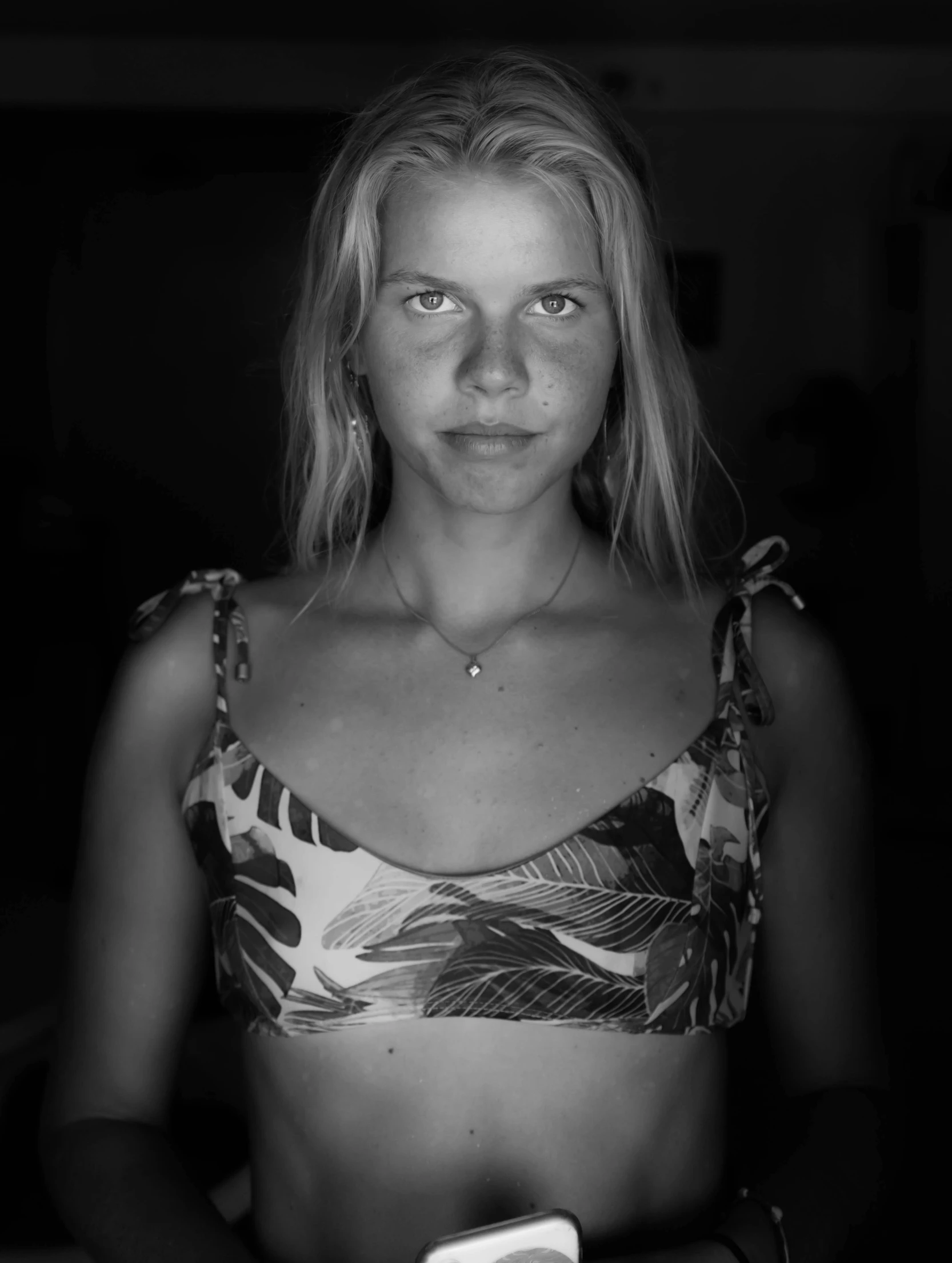 a black and white photo of a woman holding a cell phone, by Andrée Ruellan, she is wearing a black tank top, portrait top light, vacation photo, (((low light)))