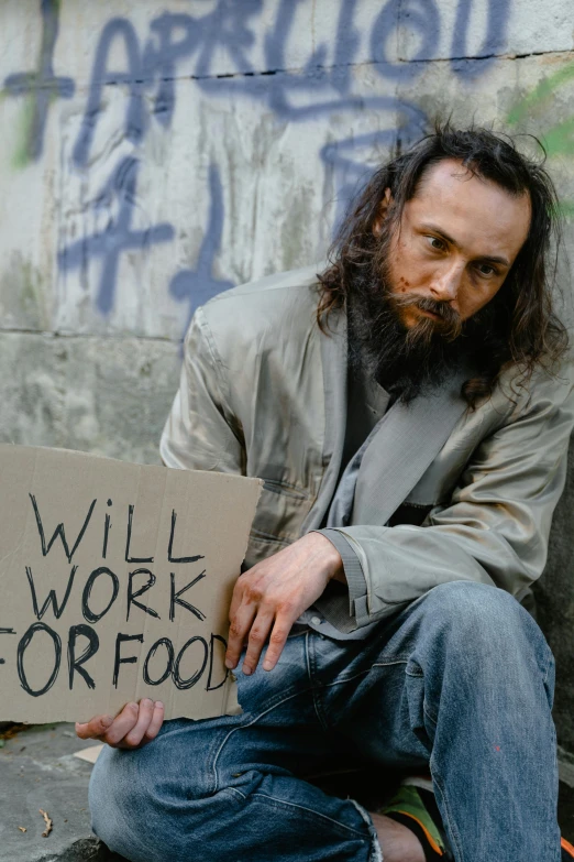 a man sitting on the ground holding a sign, by William Berra, trending on unsplash, renaissance, cyberpunk homeless, food, tommy wiseau, scruffy looking