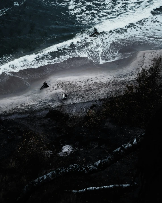 a couple of people standing on top of a beach next to the ocean, dark ocean water, from above, spooky photo, unsplash photo contest winner