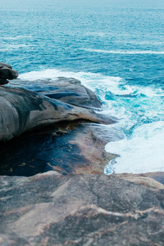 a man standing on top of a rock next to the ocean, by Elizabeth Durack, trending on unsplash, minimalism, huge veins, whirlpool, granite, whale carcass