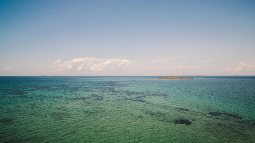 a body of water with a small island in the distance, by Nina Hamnett, unsplash, clear blue skies, green sea, overview, wide film still