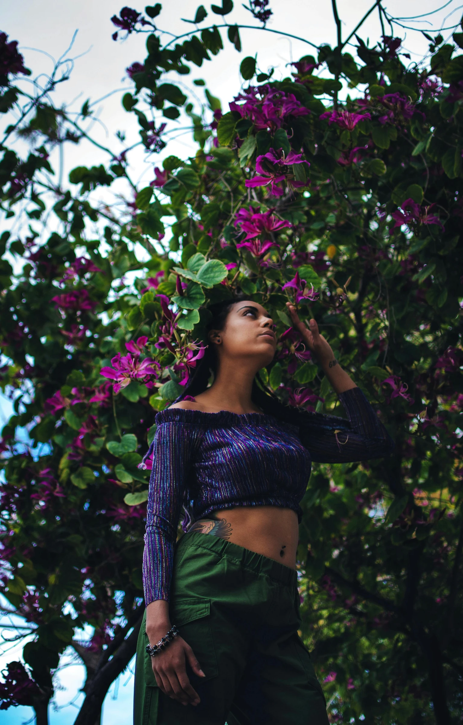 a woman standing in front of a tree with purple flowers, by Max Dauthendey, pexels contest winner, wearing crop top, tropical mood, dark-skinned, foliage clothing