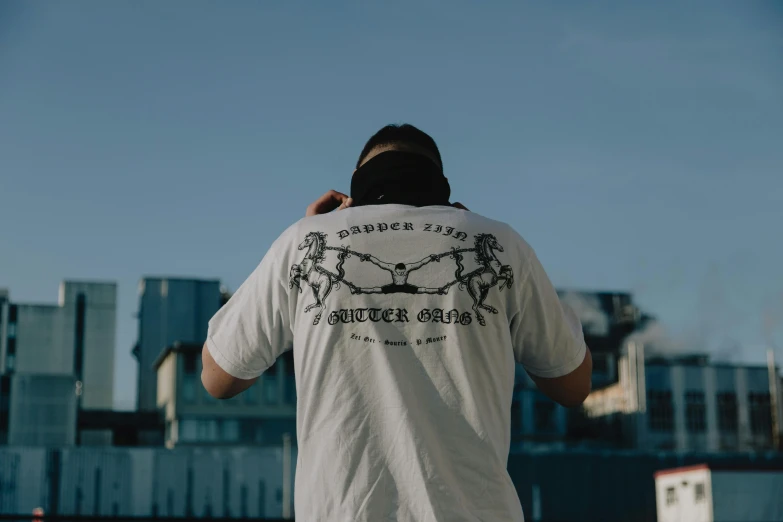 a man standing on top of a roof talking on a cell phone, a tattoo, by Daniel Seghers, pexels contest winner, graphic tees, back of head, detailed white, front side