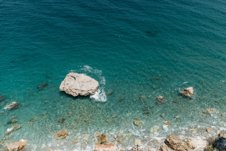 a large rock in the middle of a body of water, a picture, unsplash contest winner, minimalism, costa blanca, sparkling cove, high - angle view, detailed photo 8 k