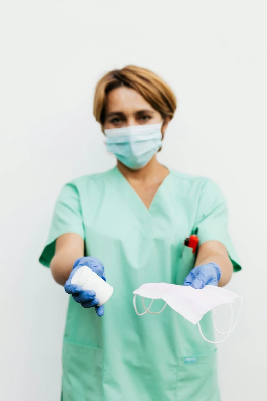 a woman wearing a green scrub suit and blue gloves, pexels, with a white, pastel', holding a stuff, virus