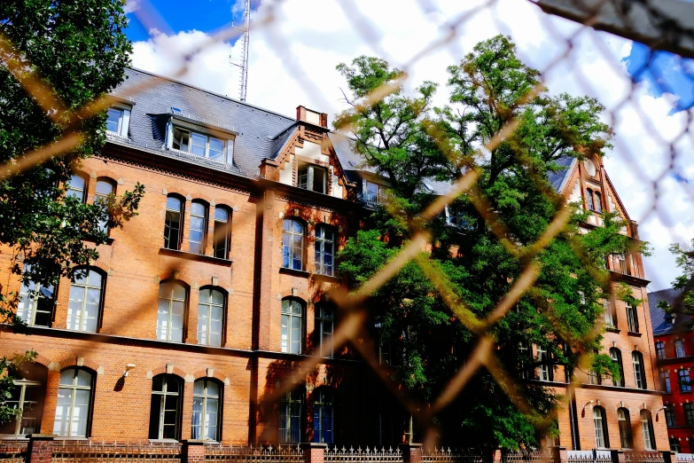 a large brick building behind a chain link fence, inspired by Albert Paris Gütersloh, unsplash, paris school, slide show, preserved historical, against the backdrop of trees, high details photo