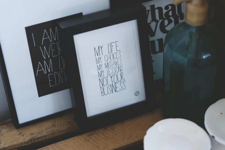 a couple of framed pictures sitting on top of a wooden table, unsplash, letterism, jar on a shelf, my little everything, product display photograph, black stencil