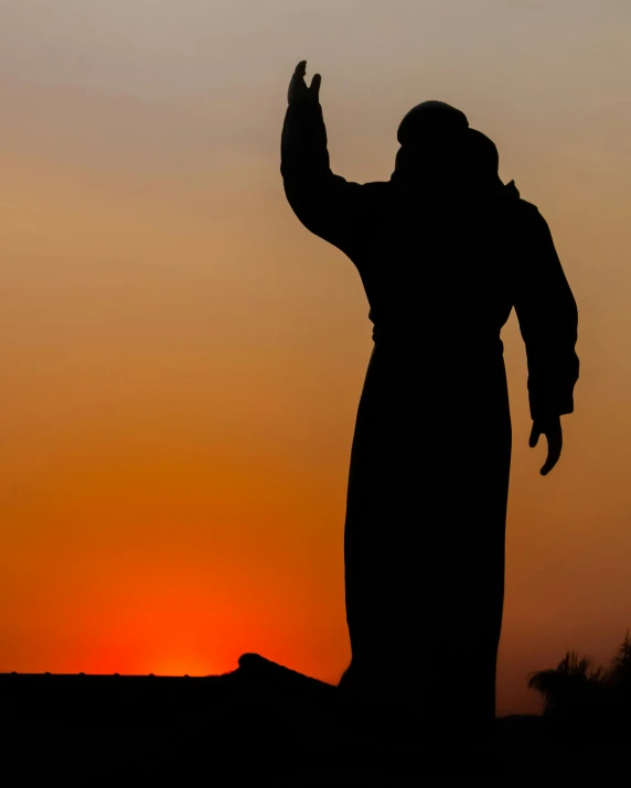 a silhouette of a person standing in front of a sunset, a statue, inspired by Pierre Puvis de Chavannes, unsplash, hurufiyya, religious robes, dabbing, museum quality photo, sheikh