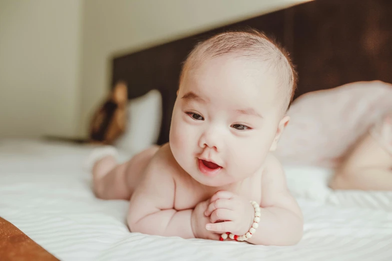 a close up of a baby laying on a bed, by Julia Pishtar, pexels contest winner, young cute wan asian face, belly exposed, jewelry, a handsome