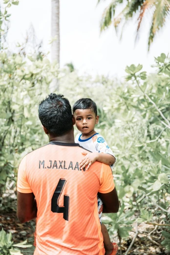a man holding a small child in his arms, pexels contest winner, sri lankan landscape, football player, with names, on an island