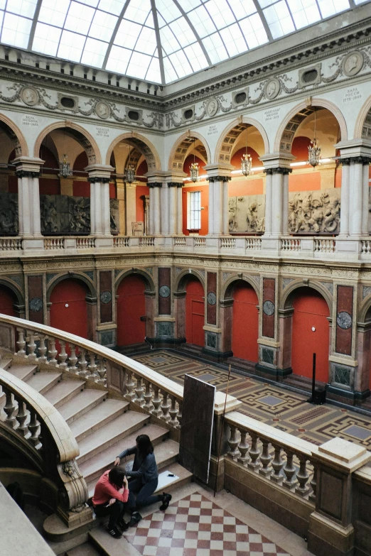 a couple of people that are sitting on some stairs, inspired by Thomas Struth, pexels contest winner, visual art, inside a grand ornate room, red building, 2 5 6 x 2 5 6 pixels, tall arched stone doorways