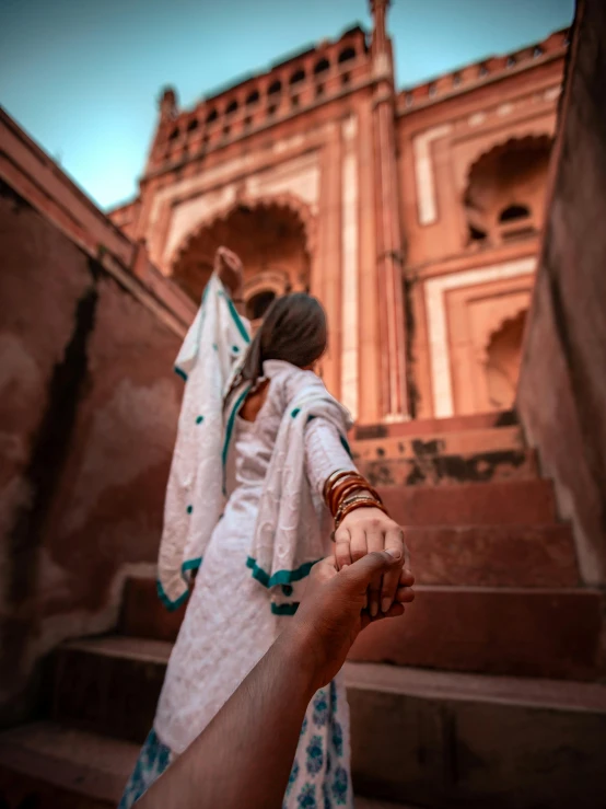 a woman holding a man's hand in front of a building, inspired by Steve McCurry, renaissance, painting of mehrangarh fort, background image, popular on instagram, thumbnail