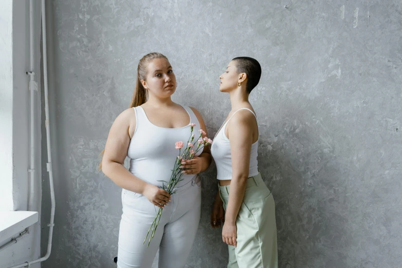 two women standing next to each other holding flowers, trending on pexels, aestheticism, an obese, leaning on the wall, wearing white leotard, upper body image