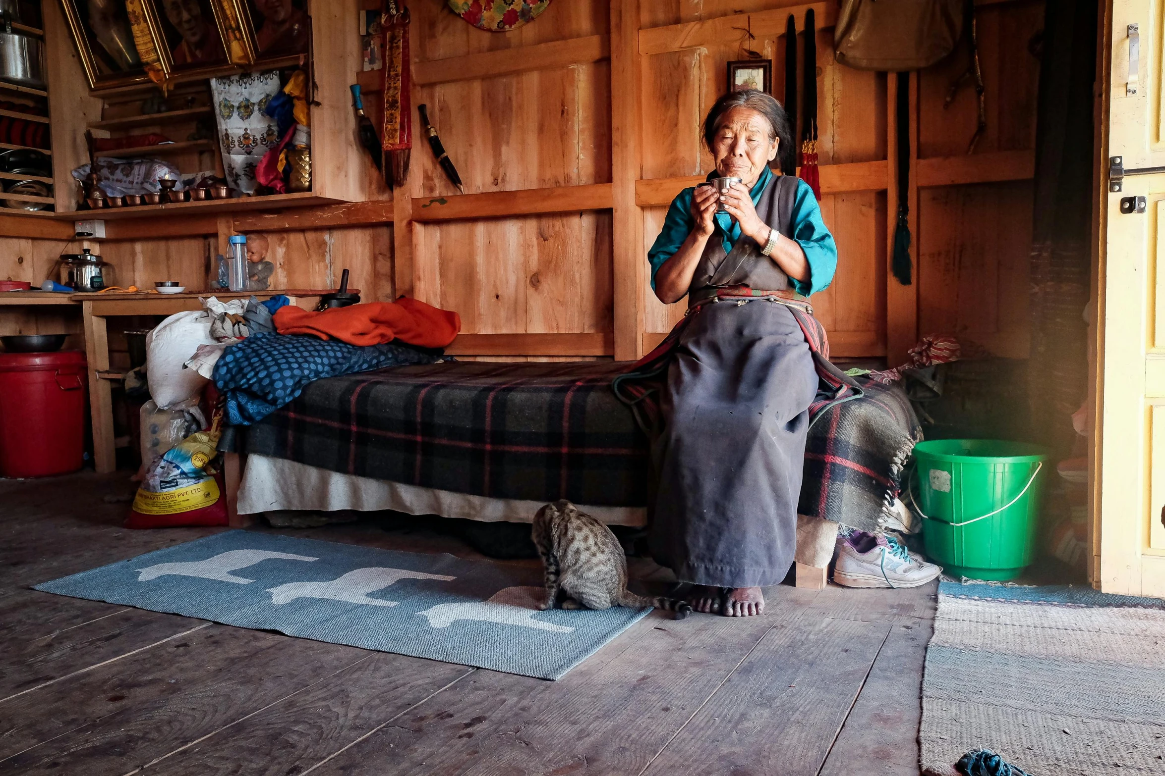 a woman sitting on a bed in a room, by Jan Tengnagel, pexels contest winner, hurufiyya, longhouse, holding a bagpipe, with small cat on lap, omar shanti himalaya tibet