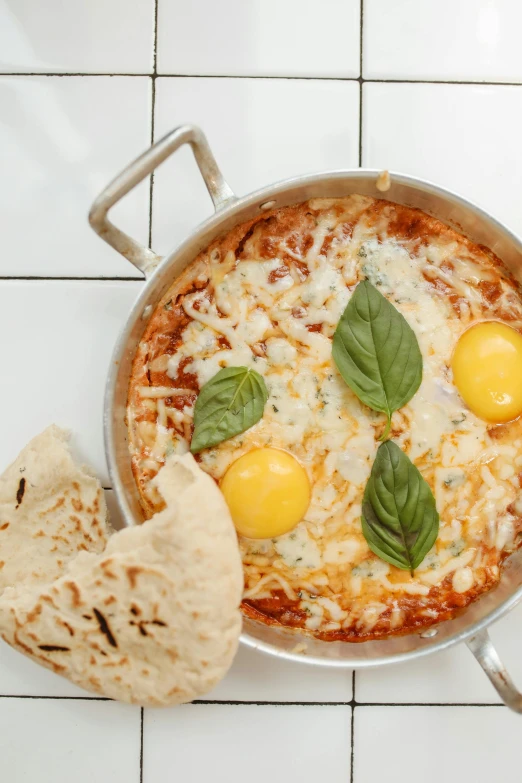 a pan filled with food sitting on top of a white tiled floor, eggs, lasagna, ameera al-taweel, mint