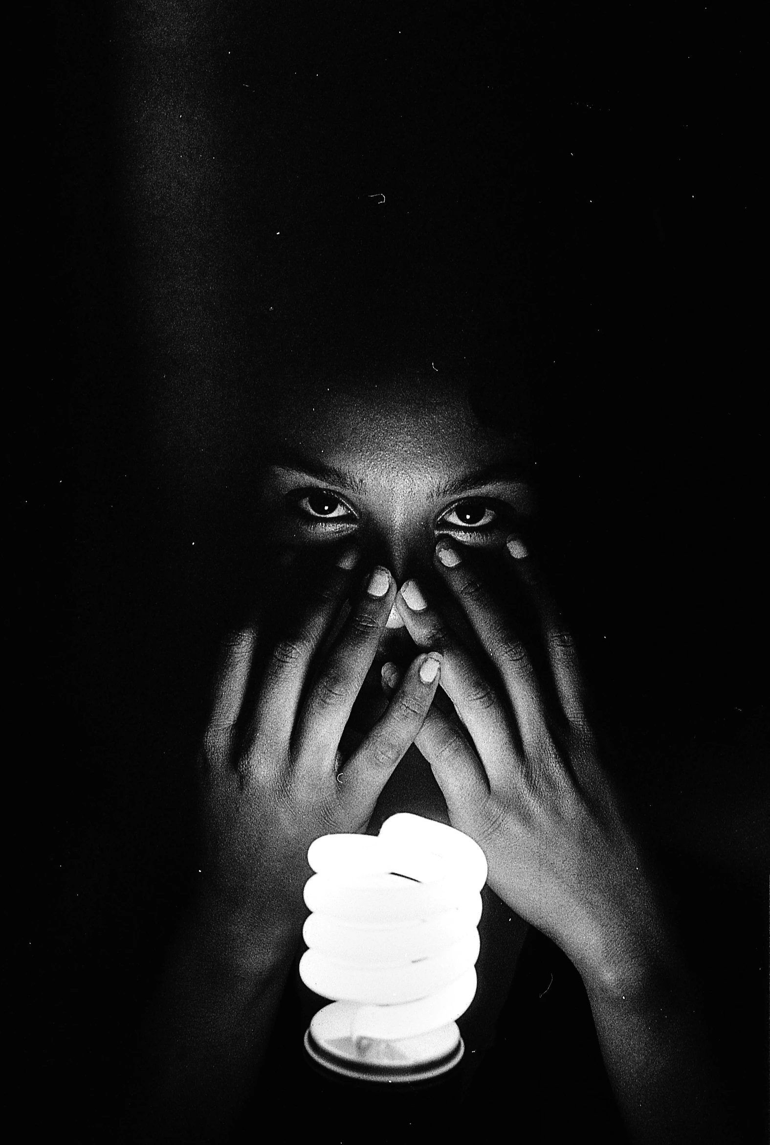 a black and white photo of a person holding a light bulb, by Alexis Grimou, hands shielding face, candle, large entirely - black eyes, malika favre