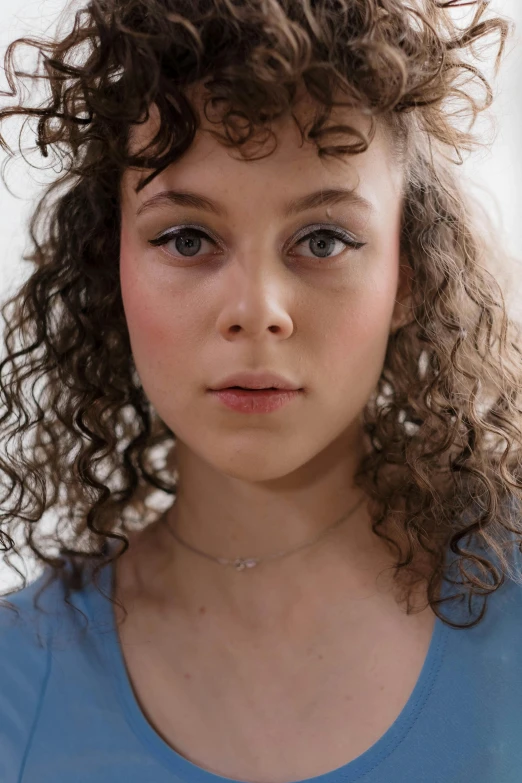 a young girl with curly hair wearing a blue shirt, inspired by Elizabeth Polunin, trending on pexels, hyperrealism, large forehead, sophia lillis, mixed race woman, sydney sweeney