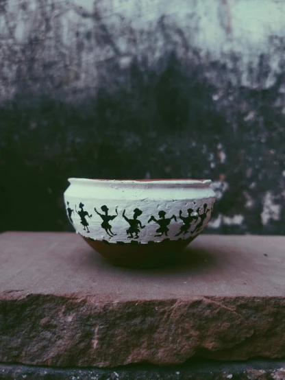 a black and white bowl sitting on top of a stone block, bengal school of art, dancing people, handcrafted, lofi, detailed product photo