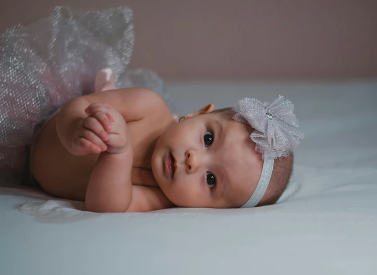 a close up of a baby laying on a bed, by Dan Luvisi, pexels, art photography, wearing a tutu, confident pose, gif, grey