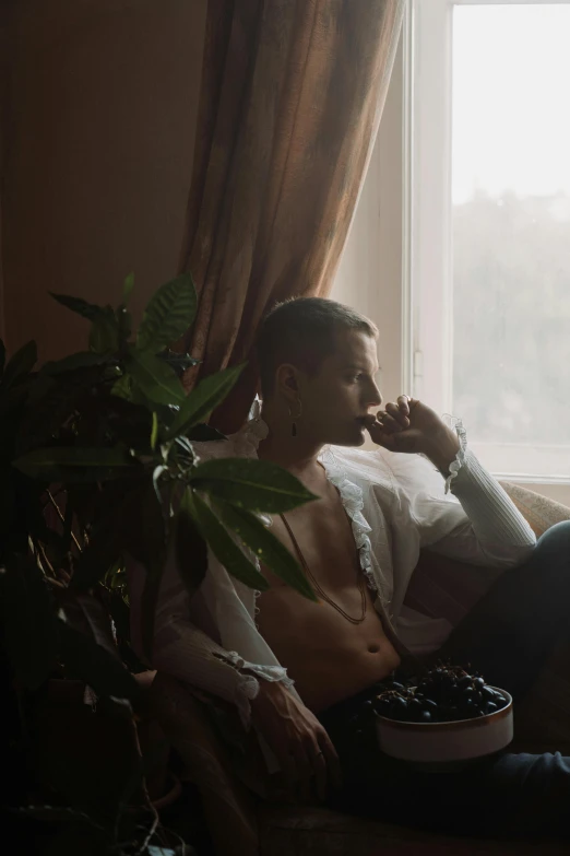 a man sitting on a couch in front of a window, a photo, inspired by Elsa Bleda, trending on pexels, renaissance, smoking body, brown buzzcut, maxim sukharev, delicate androgynous prince