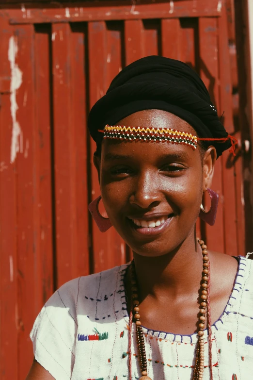 a woman standing in front of a red door, inspired by Afewerk Tekle, pexels contest winner, wearing a headband, detailed smile, ethiopian, pictured from the shoulders up