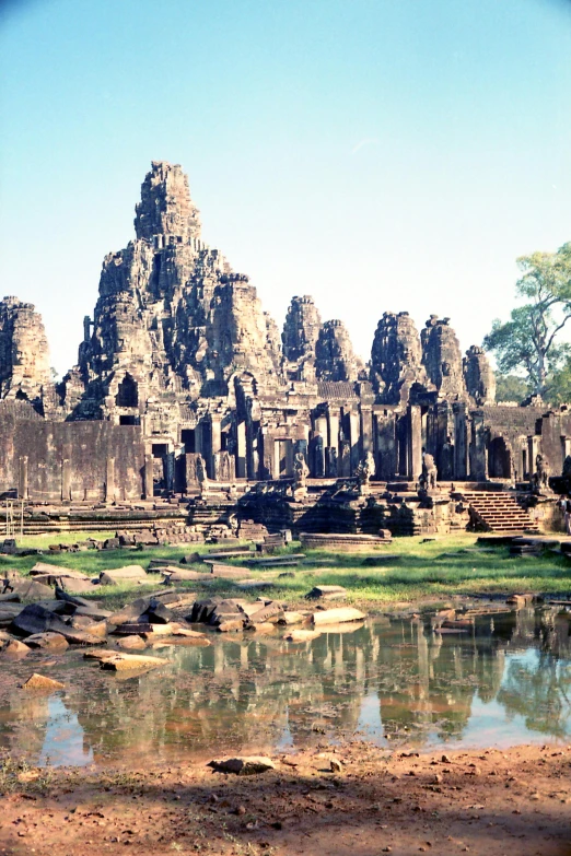 a man standing in front of a body of water, large temples, angkor, panoramic shot, ground - level view