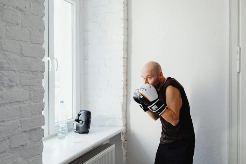 a man standing in front of a window wearing boxing gloves, by Ilya Ostroukhov, pexels contest winner, figuration libre, lifting weights, anna nikonova aka newmilky, in a fighting stance, holding a bottle