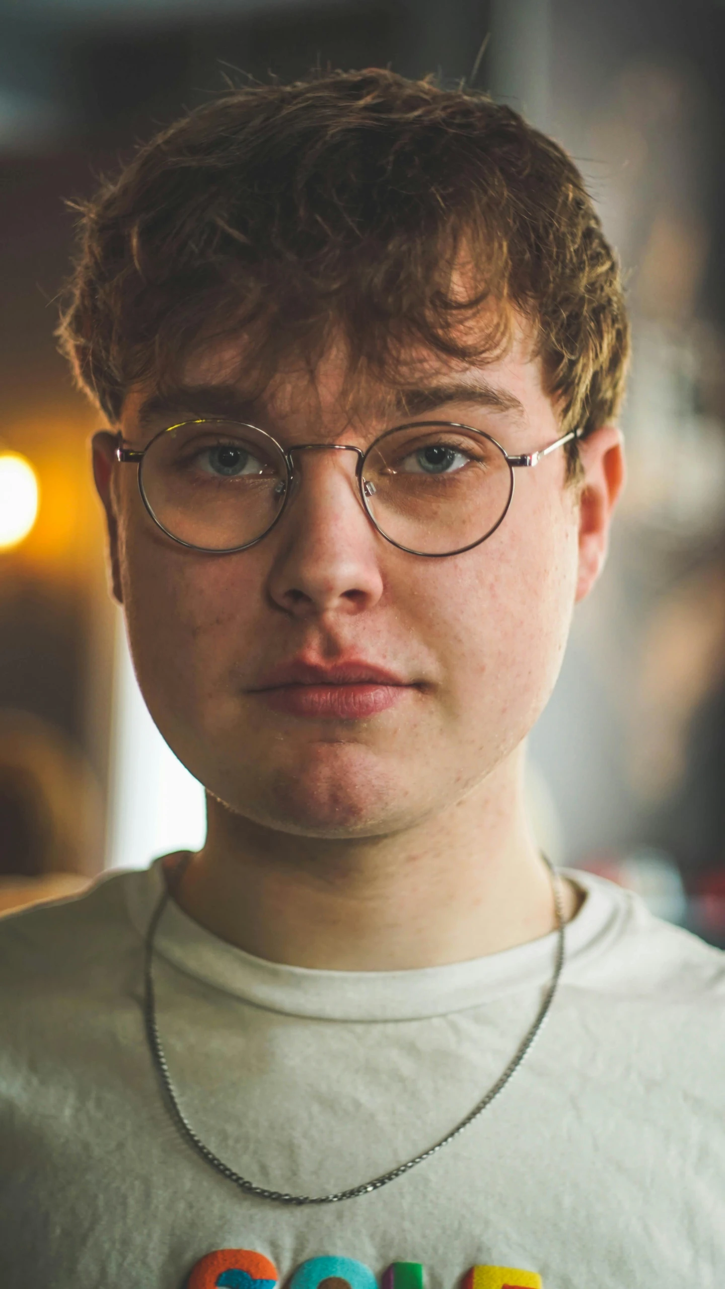 a man wearing a necklace with the word goooooooooooooooooooooooooooooooooooooooo, an album cover, by Thomas Furlong, pexels, renaissance, boyish face, round glasses, non binary model, round-cropped