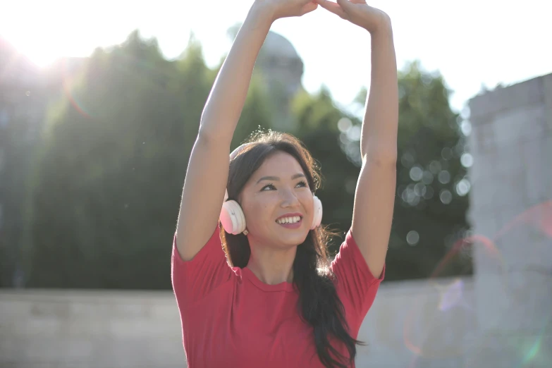 a woman with headphones standing in front of a building, pexels contest winner, happening, yoga pose, young asian girl, waving and smiling, health supporter