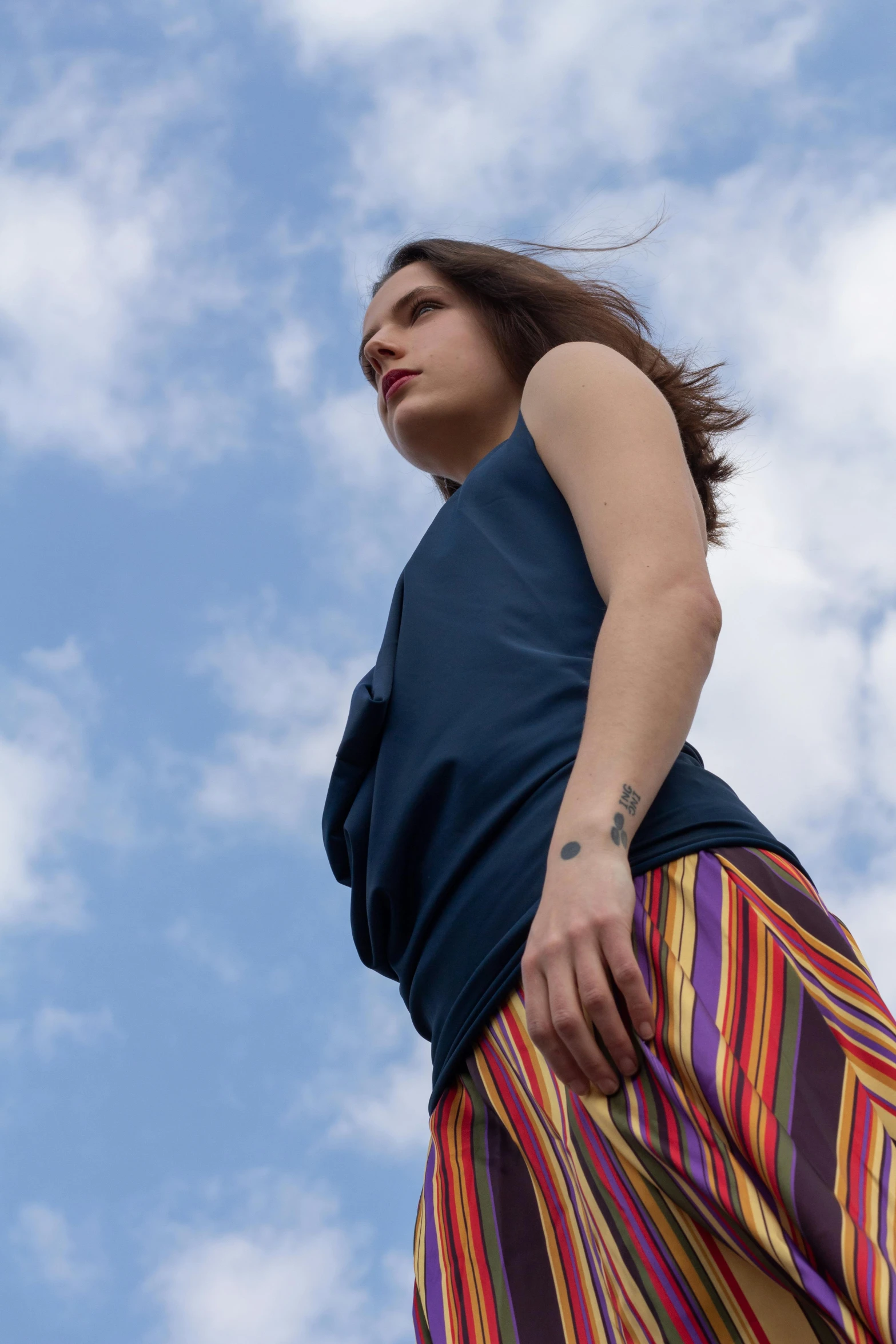 a woman standing in front of a blue sky, red tank top and wide blue pants, looking off into the distance, curated collections, multicoloured