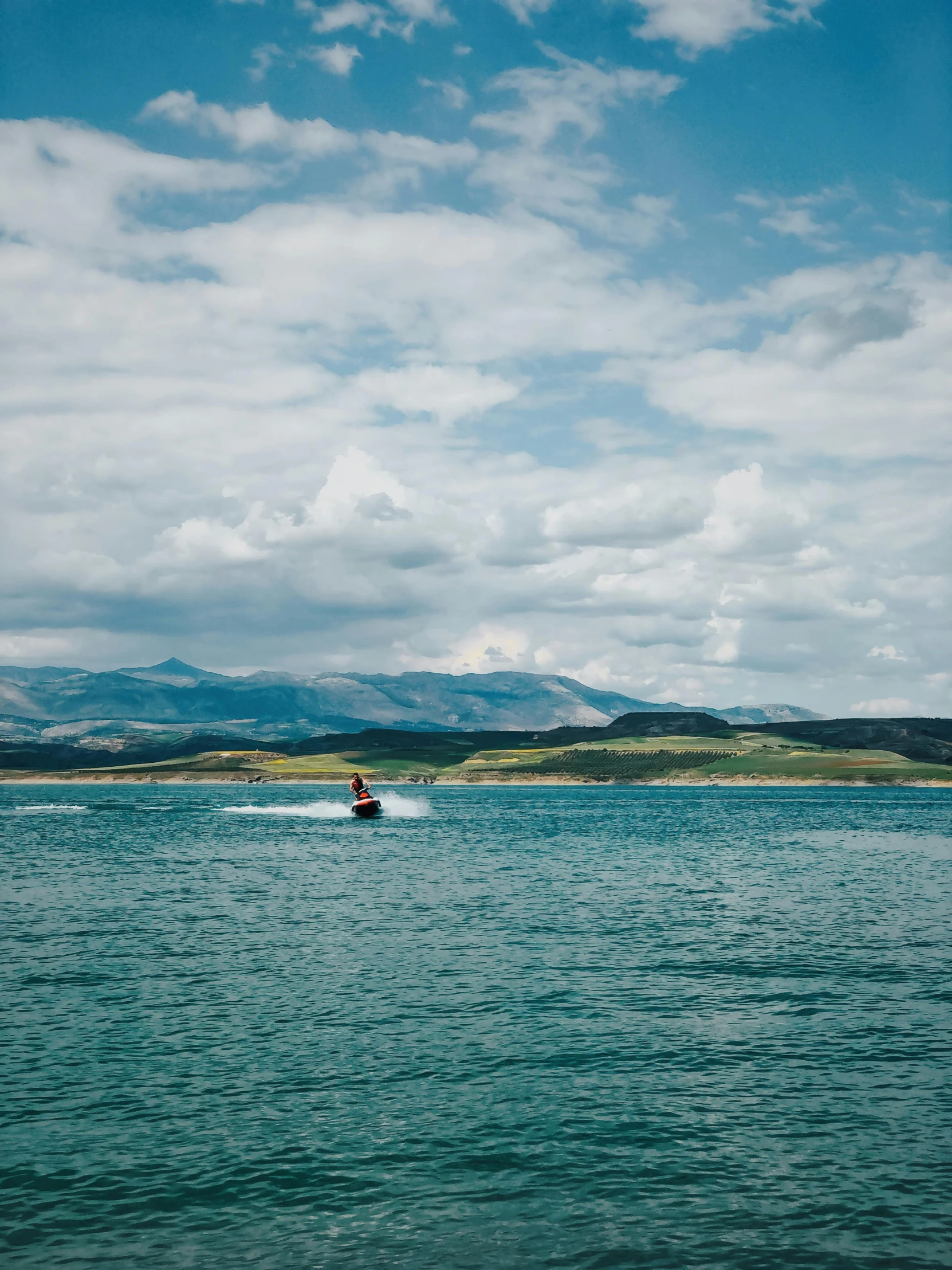 a man riding a jet ski across a lake, by Kyle Lambert, unsplash contest winner, hurufiyya, wyoming, low quality photo, distant mountains, orkney islands