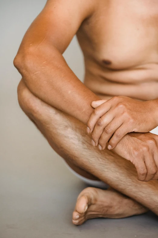 a shirtless man sitting on the floor with his legs crossed, close-up of thin soft hand, vastus lateralis, promo image, spasms