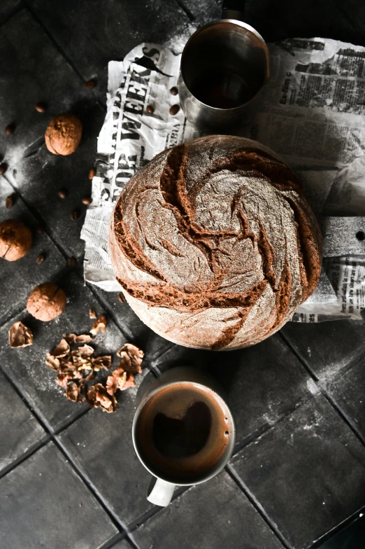 a loaf of bread sitting on top of a table next to two cups of coffee, a still life, inspired by Normand Baker, pexels contest winner, walnuts, dark bacgkground, round format, thumbnail