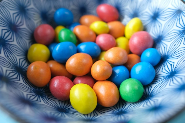 a bowl filled with colorful candy sitting on top of a table, by Joe Bowler, pexels, m & m figure, some orange and blue, pastell colours, recipe