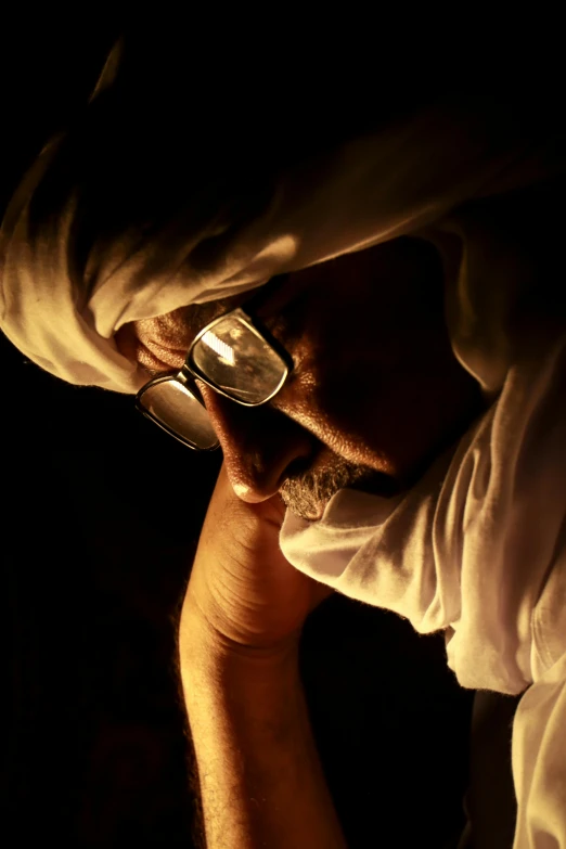 a man holding a cell phone up to his face, an album cover, inspired by Abdur Rahman Chughtai, flickr, wearing white cloths, cinematic chiaroscuro, wearing reading glasses, photographed for reuters