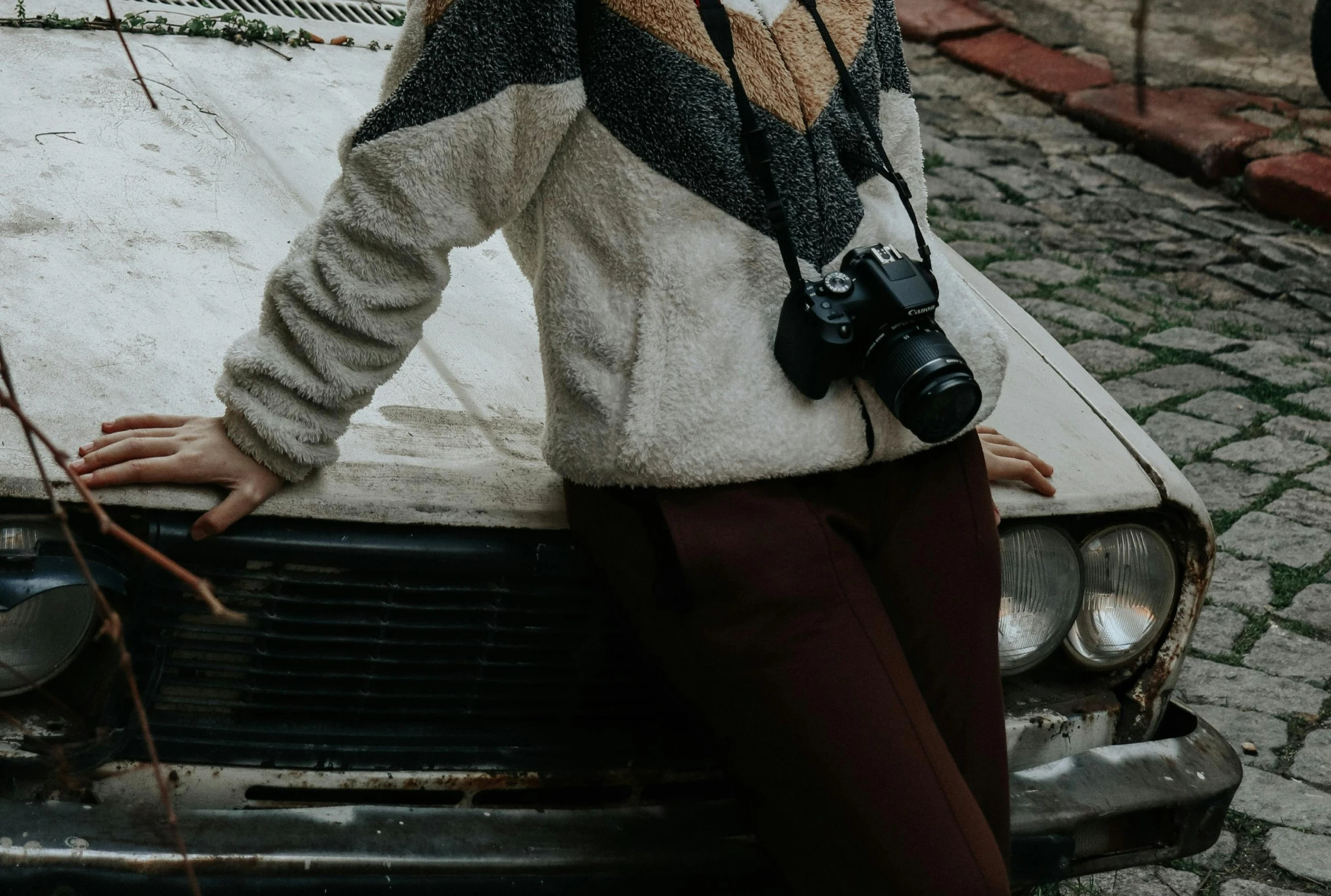 a woman leaning on the hood of a car, a picture, trending on pexels, holding a camera, wearing sweater, fullbody photo, fuzzy details