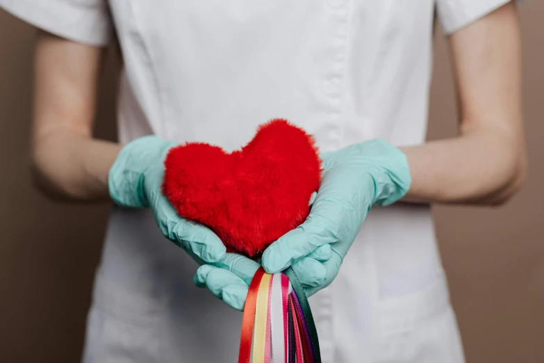 a woman in a white shirt holding a red heart, a colorized photo, pexels contest winner, surgical gown and scrubs on, rainbow accents, floggers, diagnostics