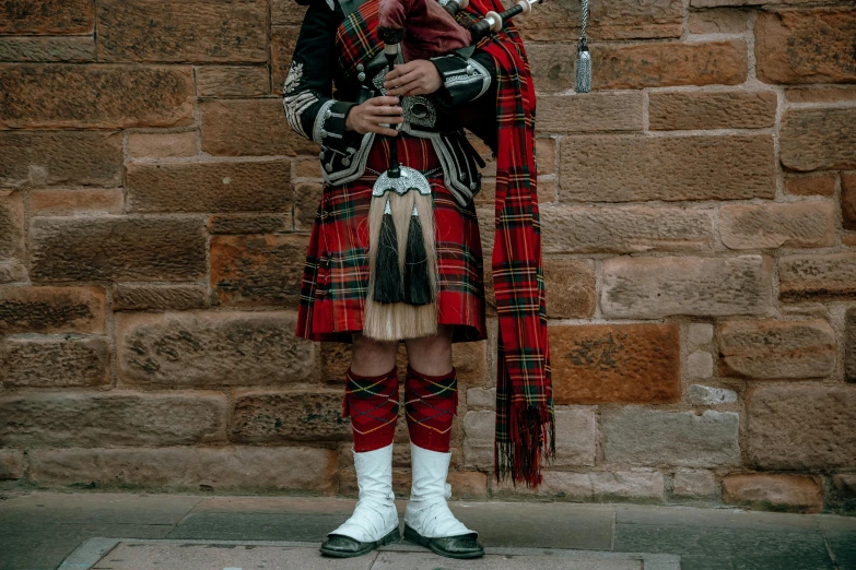 a man in a kilt standing in front of a brick wall, inspired by David Macbeth Sutherland, pexels contest winner, renaissance, glass pipes showing red, traditional costume, girl wearing uniform, concert photo