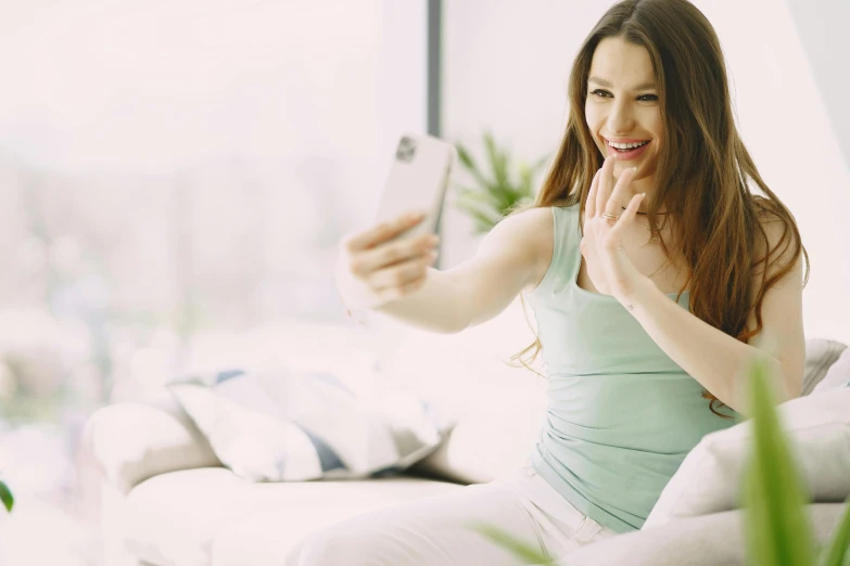 a woman sitting on a couch taking a selfie, happening, clean face and body skin, very excited, youtube thumbnail, a beautiful woman in white