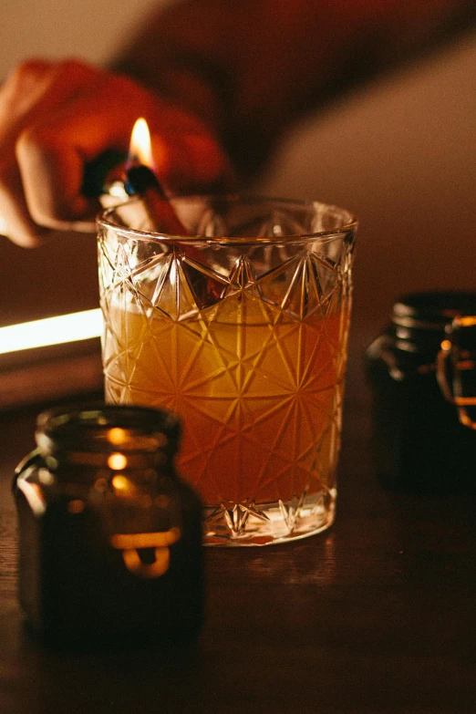 a person lighting a candle in a glass, by Lee Loughridge, unsplash, renaissance, cocktail in an engraved glass, drinking cough syrup, made of glowing oil, 2 0 yo