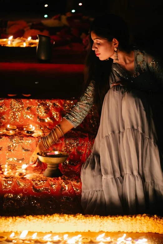 a woman lighting candles on a bed in a dark room, pexels contest winner, renaissance, dressed in a sari, glowing with silver light, promo image, idian dress