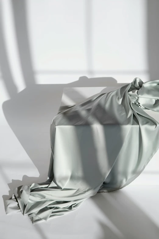 a blanket sitting on top of a white chair, an abstract sculpture, inspired by Anna Füssli, trending on unsplash, photorealism, shadow gradient, flowing silk sheets, seafoam green, satin silver