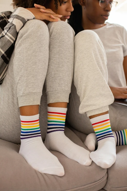 two people sitting on a couch using a laptop, inspired by Okuda Gensō, striped socks, pride month, sitting in bedroom, muted rainbow tubing