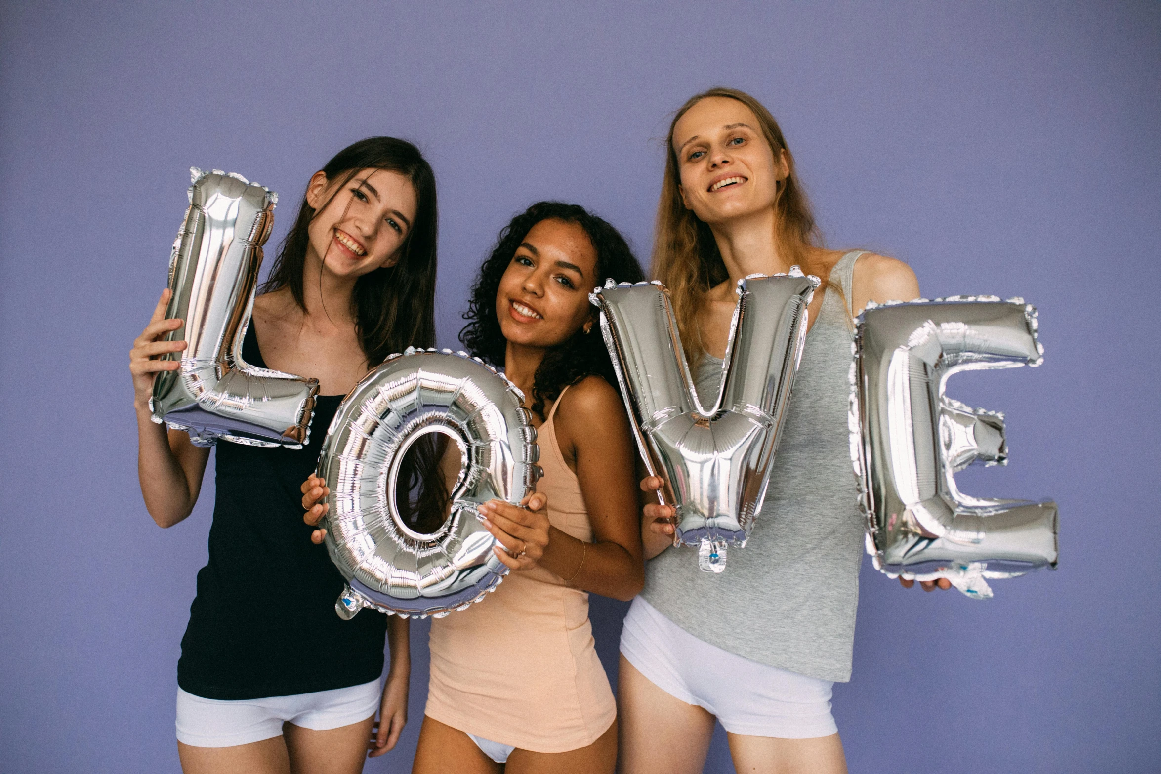 a group of three women standing next to each other, trending on unsplash, letterism, party balloons, silver accessories, love theme, product introduction photo