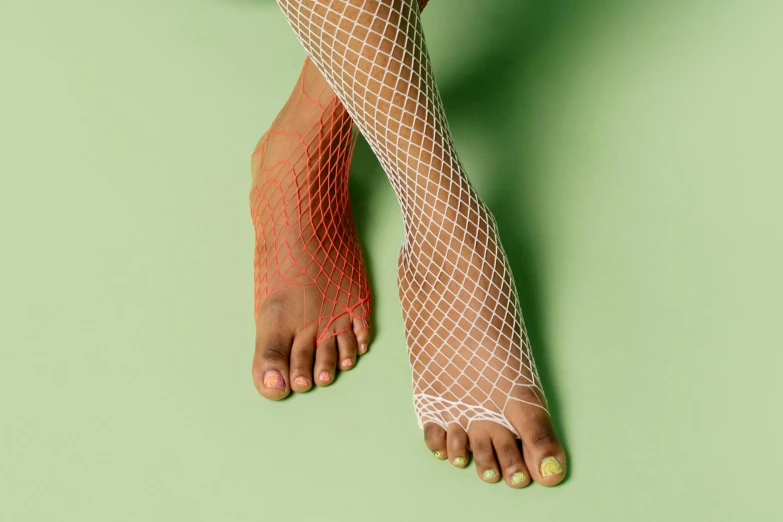 a woman's legs in fishnet stockings on a green surface, inspired by Victorine Foot, trending on pexels, hyperrealism, red and white neon, with brown skin, crochet skin, foot wraps