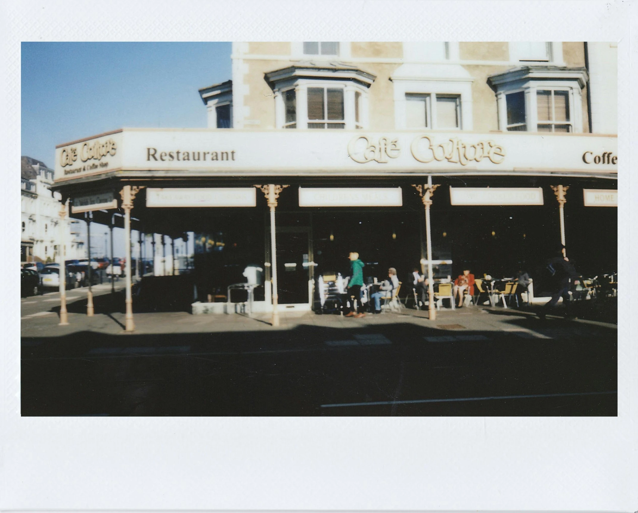 a group of people sitting outside of a restaurant, a polaroid photo, by Lee Gatch, at the seaside, old shops, colonnade, cafe for mice